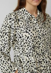 Blusa con colletto in tessuto leggero caratterizzata da un motivo astratto a macchie nere e crema; bottoni frontali, con dettaglio sulla vita arricciato.