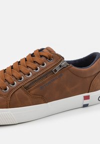 Sneaker en cuir synthétique marron avec lacets en bronze, fermeture éclair sur le côté, intérieur bleu marine et semelle en caoutchouc blanc avec des accents rouge, blanc et bleu.