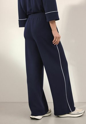 Tmavě modré kalhoty širokého střihu z měkké tkaniny s elastickým pasem, zdobené kontrastním bílým pruhovým lemováním po stranách a s uvolněným střihem.
