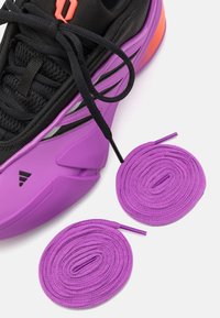Paarse sportieve schoen met een zwarte mesh bovenzijde, gebogen design en oranje accenten. Twee paarse veters liggen naast de schoen.