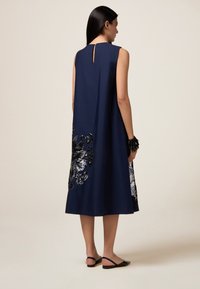 Navy ärmelloses Kleid mit Schlitzrücken, verziert mit silbernen und schwarzen Pailletten in Blumenform am Saum, glatte Stoffstruktur.