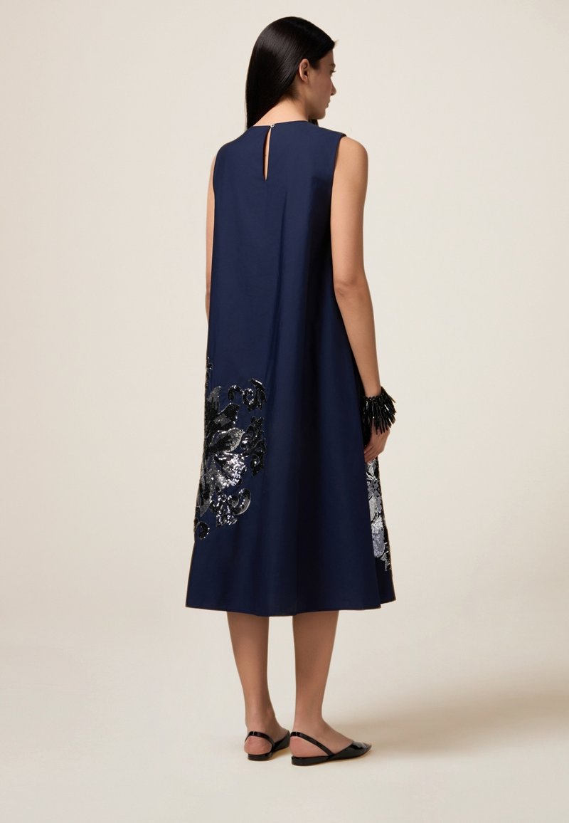 Navy ärmelloses Kleid mit Schlitzrücken, verziert mit silbernen und schwarzen Pailletten in Blumenform am Saum, glatte Stoffstruktur.