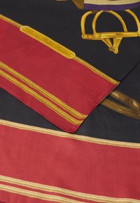 Hodvábny šál s čiernym pozadím a červenými a zlatými pruhmi, umelecké dielo zobrazujúce jazdecké vybavenie a logo v zlate.