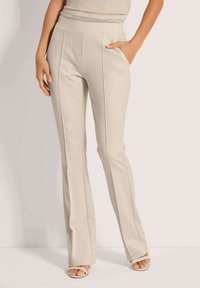 Beige flared broek met hoge taille, voorzien van zijzakken en verticale naaddetails. Gemaakt van een soepele, gestructureerde stof.