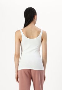 Camiseta de algodón blanca sin mangas con tirantes estrechos, diseño ajustado y dobladillo recto. Vista por detrás, combinada con pantalones de chándal rosas.