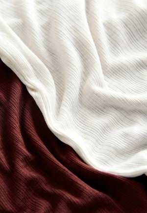 Miękka prążkowana tkanina układa się w fałdy o kontrastujących kolorach: écru i głębokim brązie, ukazując fakturę i delikatne układanie.