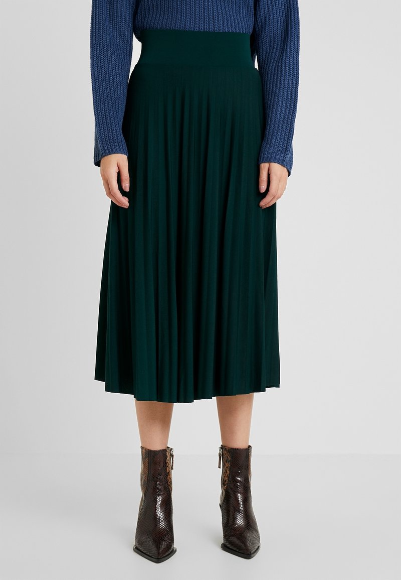 Grön plisserad midikjol med en slät midja, kombinerad med en blå texturerad stickad tröja och glänsande bruna ankelboots.