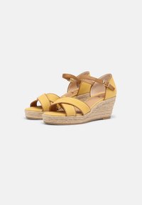 Yellow wedge sandals feature crisscross straps, ankle strap with buckle, and a textured jute-wrapped heel. Soft leather-like material.