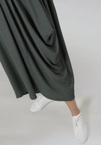 Donkergroene geribbelde midi-jurk met gedrapeerd ontwerp, gecombineerd met witte sneakers. De rok heeft een zachte textuur en een ontspannen pasvorm.