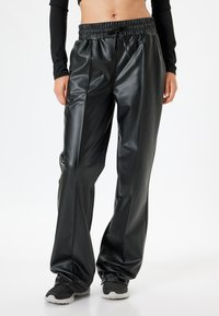 Pantaloni neri in finta pelle con vita elastica, pieghe davanti e caviglie affusolate, caratterizzati da una superficie liscia e lucida.