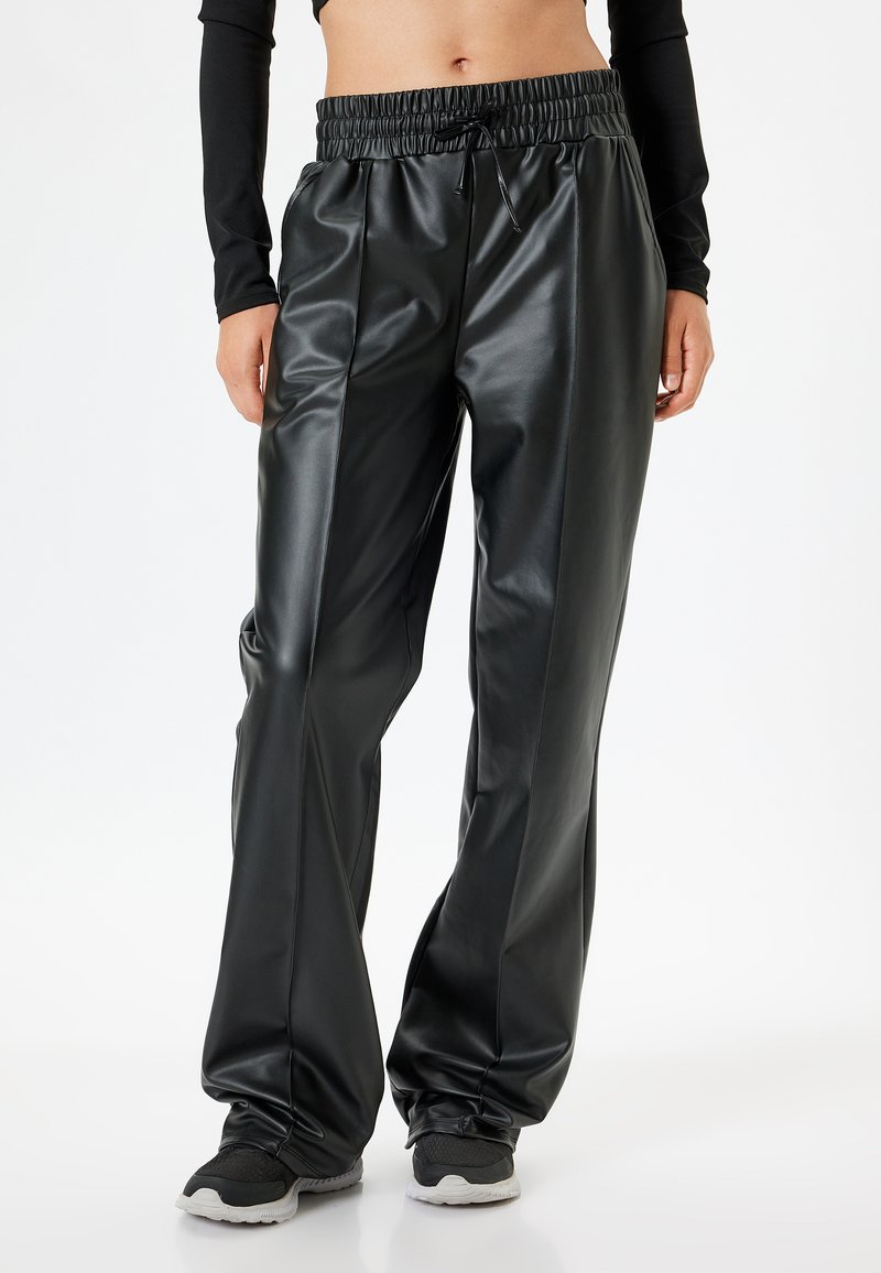 Pantaloni neri in finta pelle con vita elastica, pieghe davanti e caviglie affusolate, caratterizzati da una superficie liscia e lucida.