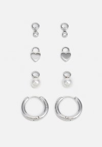 Tres pares de pendientes de plata: aros cortos con piedras transparentes, charms en forma de corazón y pendientes grandes de aro con un acabado texturizado.
