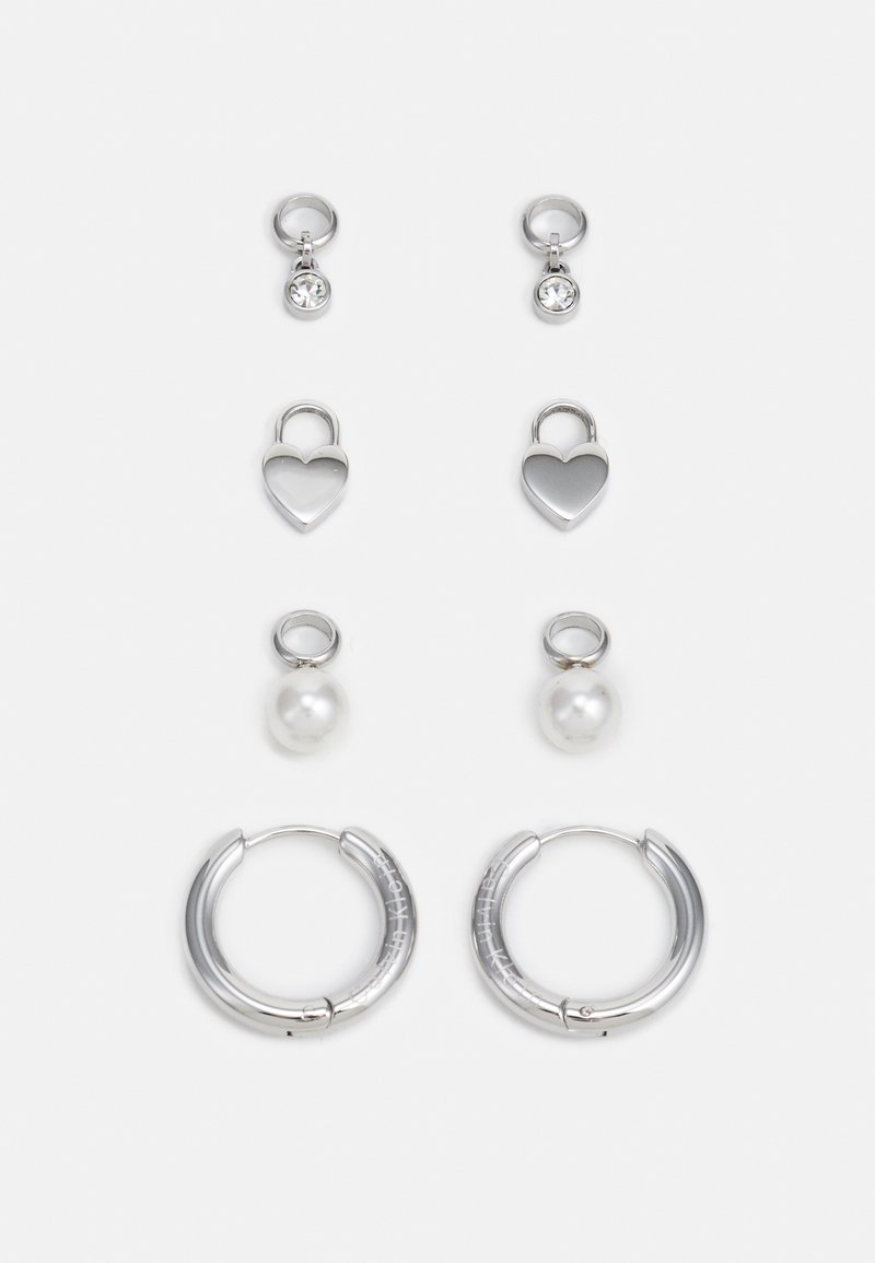 Tres pares de pendientes de plata: aros cortos con piedras transparentes, charms en forma de corazón y pendientes grandes de aro con un acabado texturizado.