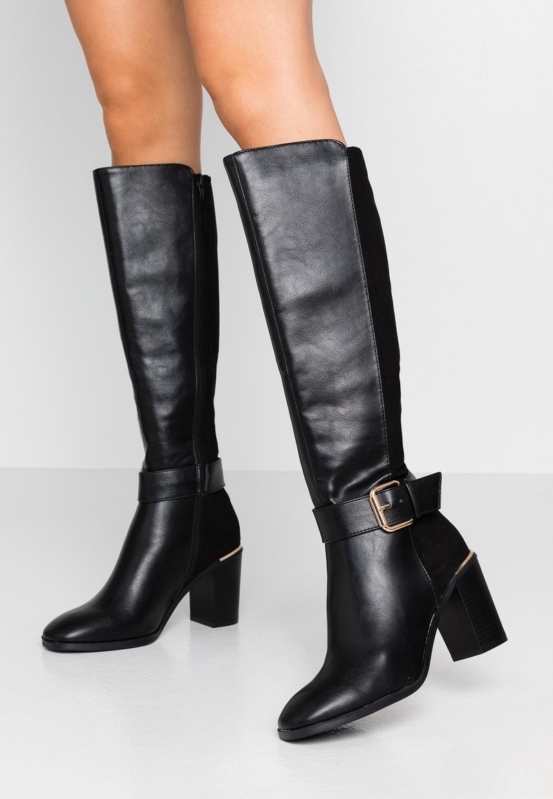 Black knee-high boots made of leather and suede, featuring a chunky heel and an ankle strap with a metal buckle detail.
