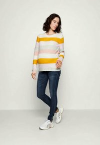 Sweater listrado com tons de amarelo, rosa e cinza, feito de material suave com um ajuste descontraído. Combinado com jeans de denim escuro e sapatilhas brancas.