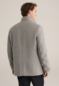 Pánsky šedý vlnený kabát s vysokým golierom, priliehavým strihom, viditeľným prešívaním a hladkou textúrou. Čistý dizajn bez ozdôb.