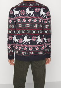 Mörkblå stickad tröja med julmotiv, prydd med vita renar, snöflingor och ett geometriskt mönster i röd och grön.