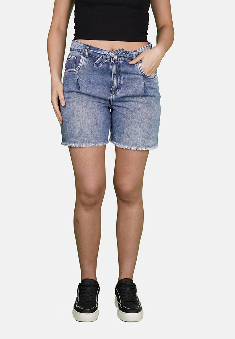 Shorts in denim con una vestibilità a vita media, colore azzurro chiaro, orlo sfilacciato, quattro tasche e un dettaglio con fiocco in vita. Abbinati a sneakers nere.