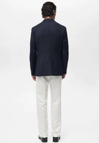 Granatowa marynarka o dobrze dopasowanym kroju, z pojedynczym rozcięciem z tyłu, noszona na kremowych spodniach, uzupełniona czarnymi butami.