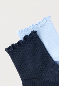 Δύο ριμπ πλεκτές κάλτσες με βολάν στις άκρες, μία ανοιχτού γαλάζιου και μία σε ναυτικό μπλε, τοποθετημένες η μία πάνω στην άλλη σε ανοιχτό φόντο.