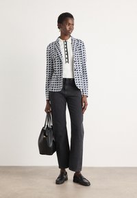 Blazer in blu scuro e bianco con motivo geometrico, maglietta bianca a coste con bottoni neri, jeans neri a gamba dritta, borsa nera e mocassini.