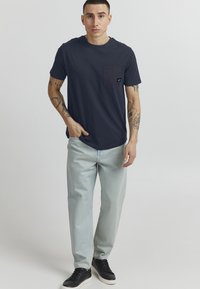 Mørkeblå bomull t-skjorte med brystlomme, kombinert med lyseblå jeans og svarte joggesko. Minimalistisk design, korte ermer og en avslappet passform.