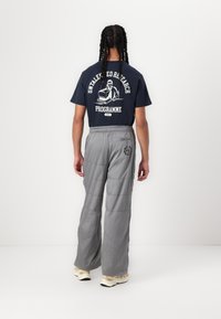 Marineblå grafisk T-shirt med hvid tekst og illustration. Grå brede bukser har en kviltet tekstur og sidelomme med logo. Letvægts sneakers.