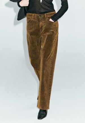 Pantaloni in velluto a coste marroni con design a gamba dritta, dotati di tasche frontali e vita con bottone, abbinati a un top nero.