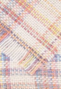 Couverture tissée avec une base crème, présentant un motif à carreaux multicolores en orange, jaune et lavande. Bords frangés ajoutant de la texture.