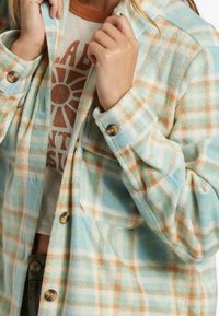 Flannel shirt in pastel blue, orange, and white plaid pattern, featuring a button closure, long sleeves, and a soft, textured fabric.
