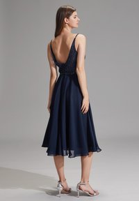 Une robe bleu marine avec un dos en V profond, un body orné et une jupe en chiffon fluide. Associée à des sandales à talons argentées.