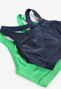 Twee sportbeha's, één marineblauw en één groen. Beide hebben een soepel materiaal, brede banden en een naadloos ontwerp. De groene heeft een gestructureerde rand.