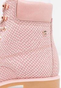 Botte cheville rose texturée avec motif hexagonal, œillets en or rose, col rembourré et semelle marron clair.