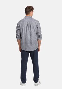 Camicia a righe blu e bianca, con una vestibilità morbida, maniche lunghe e dettagli di pieghe sul retro. Abbinata a pantaloni scuri e sneakers.