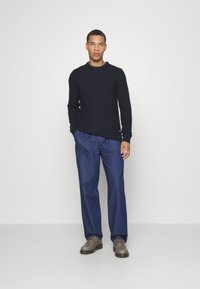 Navy knitted sweater with a textured pattern, paired with loose-fitting dark blue denim pants and gray lace-up shoes.