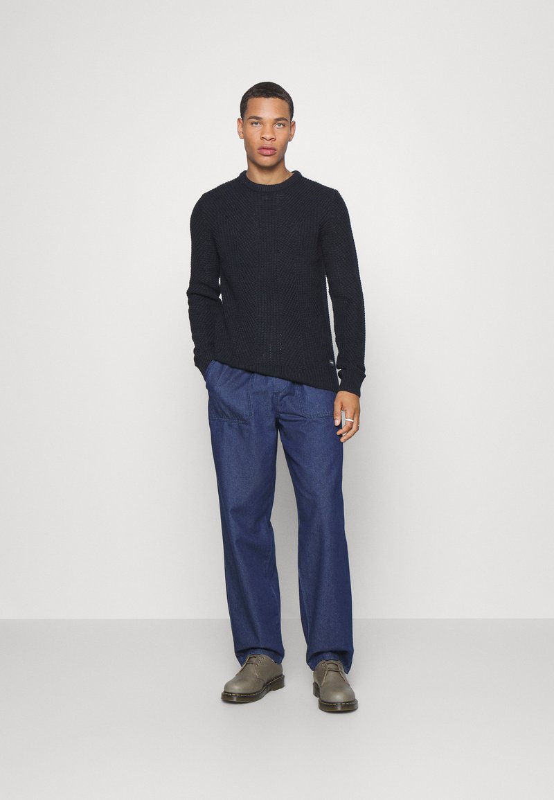 Navy knitted sweater with a textured pattern, paired with loose-fitting dark blue denim pants and gray lace-up shoes.