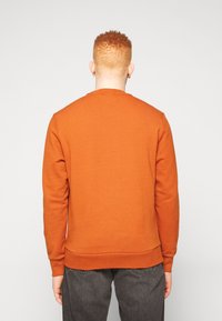 Sudadera naranja con cuello redondo, puños y dobladillo acanalados. El material parece suave y texturizado. Mostrada desde atrás.