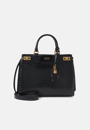 Sac à main en faux cuir crocodile noir avec poignées sur le dessus, ferrures dorées, breloque cadenas et bandoulière amovible sur un fond uni.