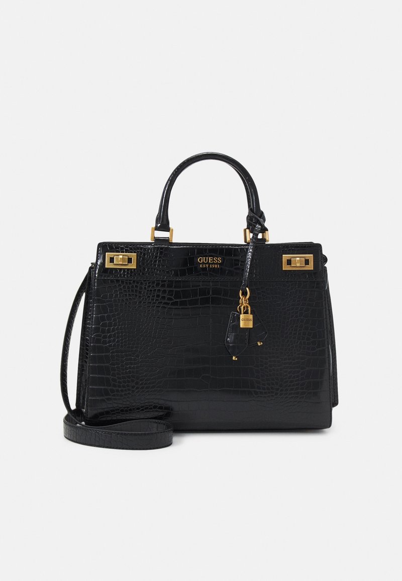 Sac à main en faux cuir crocodile noir avec poignées sur le dessus, ferrures dorées, breloque cadenas et bandoulière amovible sur un fond uni.
