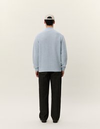 Maglioncino azzurro chiaro lavorato a maglia con orlo a coste, indossato sopra jeans scuri. Il maglione presenta un colletto alto ed è abbinato a un cappellino da baseball neutro.