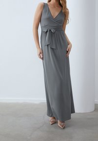 Harmaa, hihaton maksimekko, jossa syvä V-pääntie ja kietaisumalli, vyötäröllä solmittu. Sileä, virtaava kangas, kevyt tuntuma.