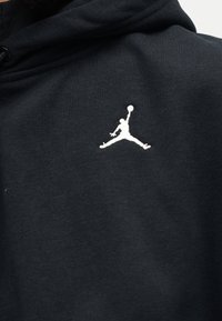 Μαύρο ύφασμα με μικρή λευκή σιλουέτα ενός ατόμου που πηδάει και απλώνει τα χέρια προς τα πάνω κρατώντας μια μπάλα μπάσκετ στην περιοχή του στήθους.