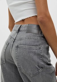 Vaqueros de mezclilla gris de cintura alta, con cinco bolsillos y una etiqueta de cuero con la inscripción "PULL&BEAR" en la parte trasera de la cinturilla. Textura sutil.