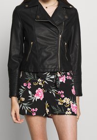 Giubbotto da motociclista in pelle nera con zip argentate e accenti dorati; texture a righe sulle maniche. Abbinate a pantaloni corti con stampa floreale.