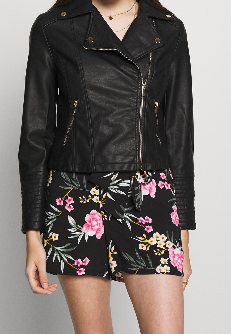Giubbotto da motociclista in pelle nera con zip argentate e accenti dorati; texture a righe sulle maniche. Abbinate a pantaloni corti con stampa floreale.
