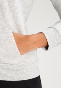 Lichtgrijze sweatshirt met een gestructureerde afwerking, voorzien van een kangoeroezak en ribbelmanchetten. De stof voelt zacht en casual aan.