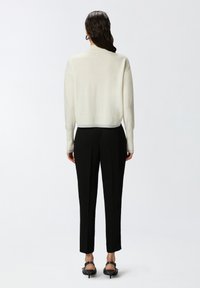 Ljuskrämfärgad tröja med ribbad nederkant och ärmslut, tillsammans med svarta skräddarsydda byxor med slim fit och elegant design. Sandaler med små klackar.