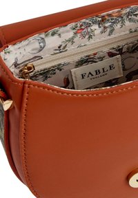 Braune Lederhandtasche mit einem goldenen Verschluss, ausgestattet mit einem blumengefütterten Innenraum und einem Reißverschlussfach. Glatte Textur mit strukturiertem Design.