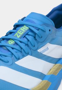 Μπλε αθλητικό παπούτσι με υφή από συνθετικό υλικό, λευκές ρίγες και μια νεόν πράσινη ετικέτα "4D ZERO". Ορατή χρυσή λεπτομέρεια στη σόλα.