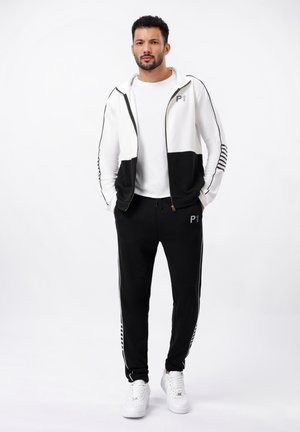 Men's tracksuit with a white and black zip-up jacket featuring a printed logo, paired with black joggers, accented with white stripes.